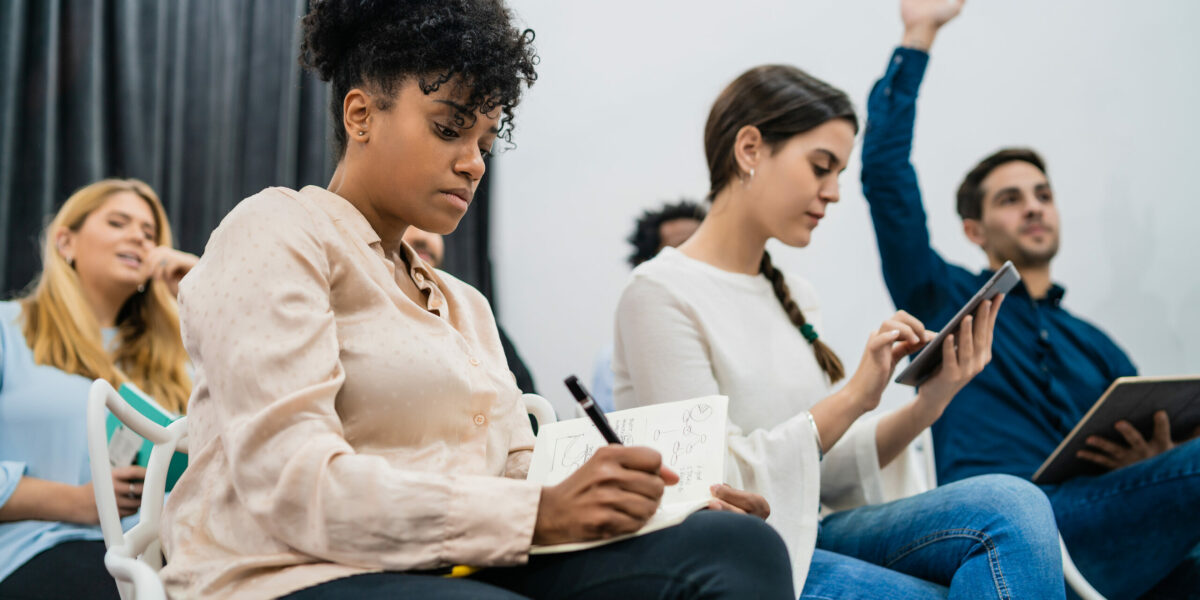 Group of young people sitting on conference together while raising their hands to ask a question. Business team meeting seminar training concept.